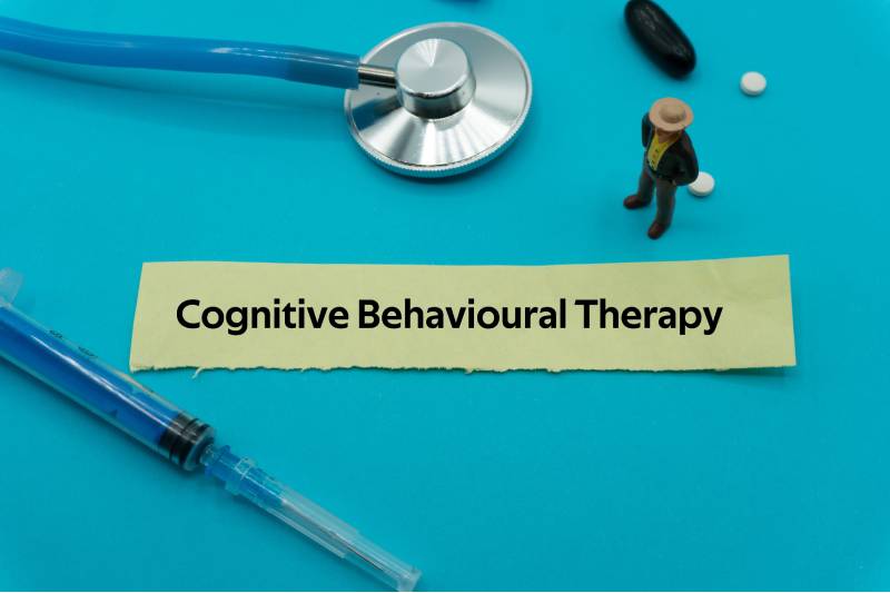 The term cognitive behavioural therapy displayed on a blue background with a needle and stethoscope kept around.