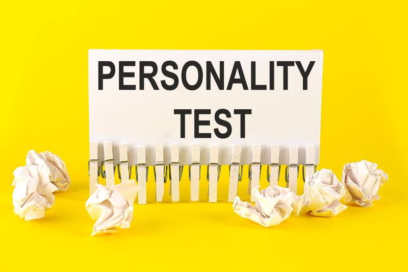 The term personality test written on a white paper placed on a yellow background and few crushed paper bits around it.