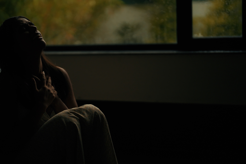 A woman sitting alone indoors, crying and feeling tense.