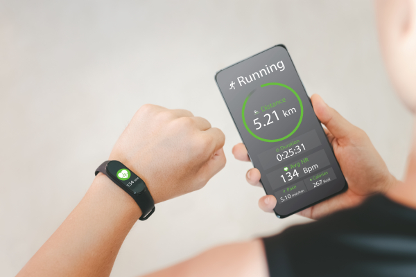 Person tracking heart rate and running status on a smartphone with a fitness tracker, optimizing workouts for better results.