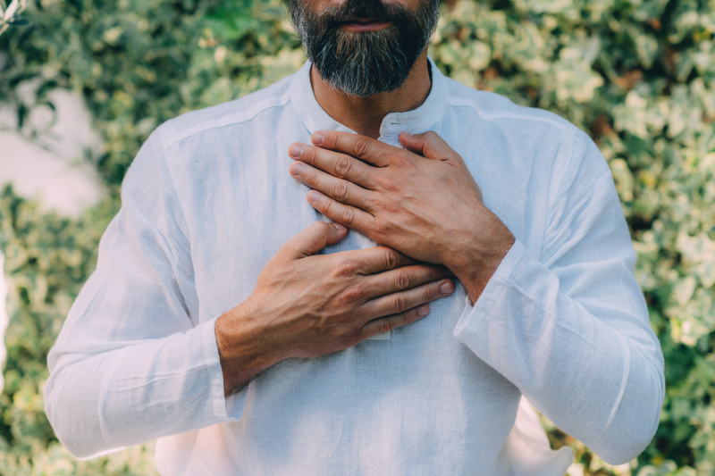 A man in a white shirt, hands in prayer position, standing in nature, embodying a self-healing moment.