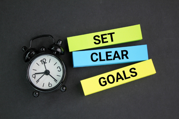 An alarm clock and sticky notes with "Set, Clear, Goals" written on a dark surface.