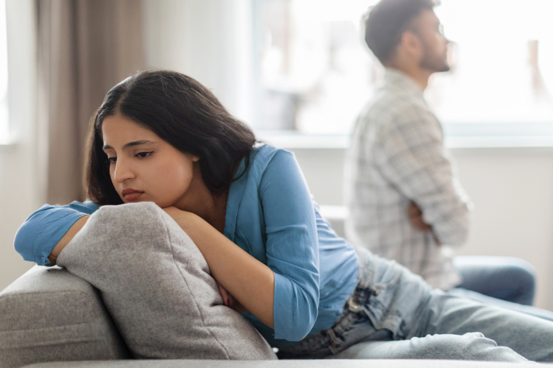 Upset couple sitting apart on a bed, symbolizing the importance of healthy discussions about mental health and finding solutions.