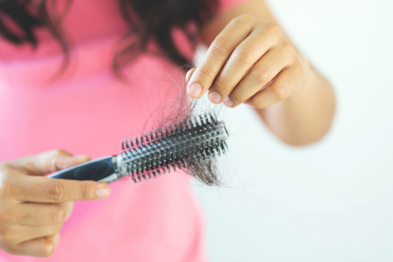 Woman in a pink T-shirt combing her hair as it falls out due to nutritional deficiencies.