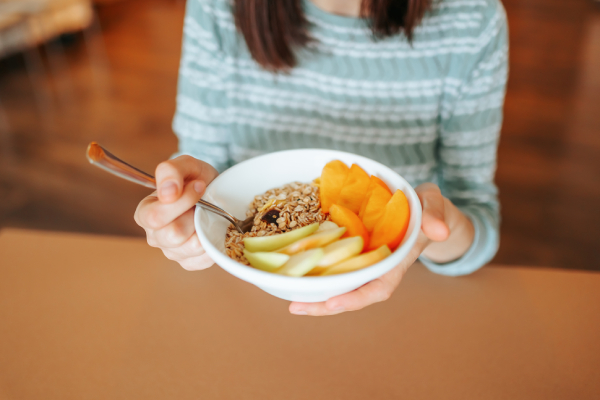 A woman holding a bowl of apples, orange slices, and a spoon, symbolizing a balanced diet for the Mesomorph body type.