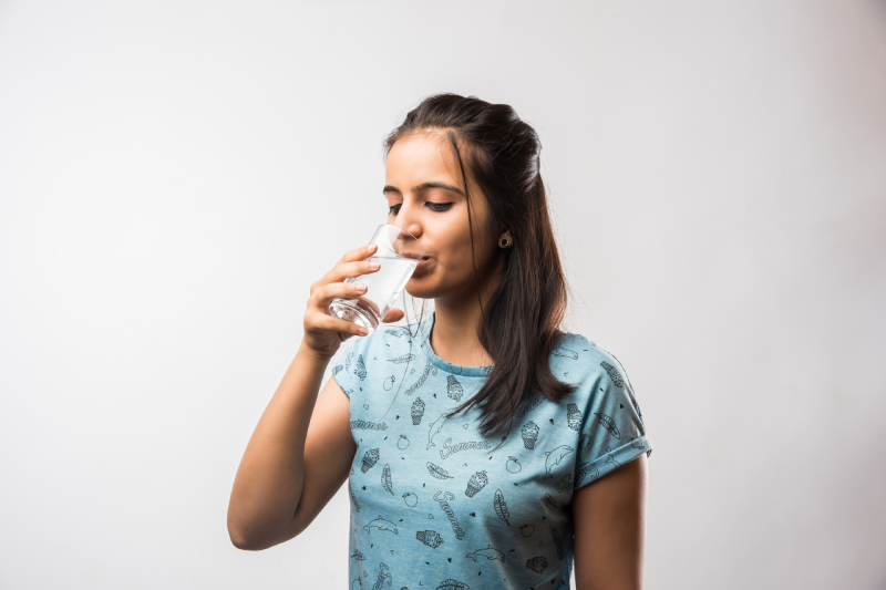 A young woman in a blue printed t-shirt drinks water, promoting hydration to support toxin removal and organ health.