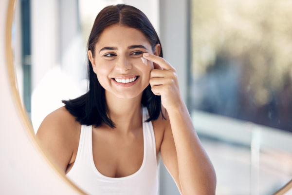 A happy young girl applies cream, looking in the mirror and reflecting self-care routines that support mental wellness.