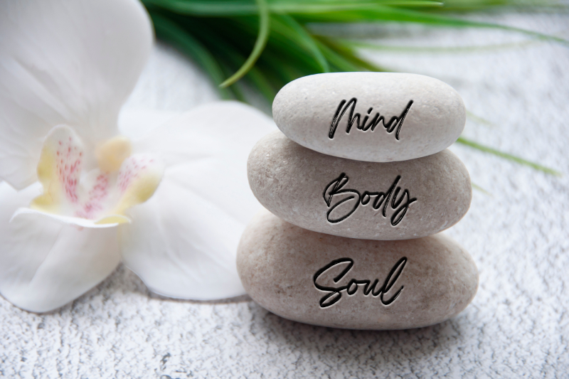 A flower and stones labeled 'Mind,' 'Body,' and 'Soul' on a table, symbolizing a holistic approach to personalized care.