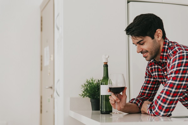 A cheerful man in a modern kitchen holds a red wine glass, with a bottle nearby, symbolizing heart and liver risks.