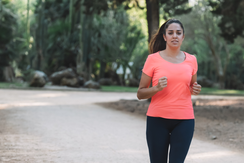 A woman jogging in the park, promoting the benefits of 30 minutes of daily exercise and avoiding prolonged sitting for better health.