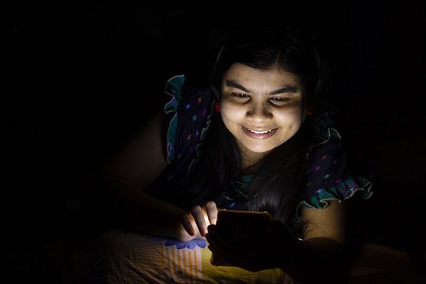 A girl using her mobile phone at night in bed, emphasizing the need to ensure 7 to 8 hours of quality sleep every night for good health.